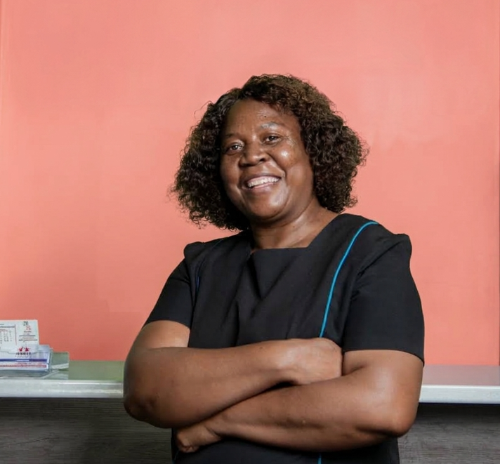 Tiny Mdungwane, the cleaner at Mahikeng Medical Center, smiling with arms crossed in a black uniform